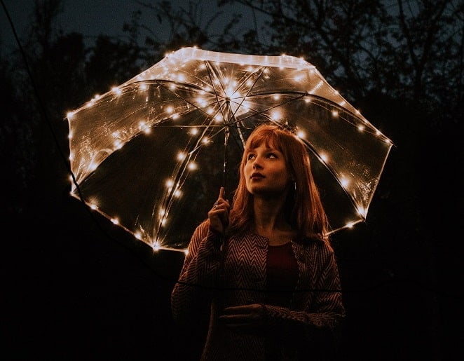 Nainen valaistun sateenvarjon alla.