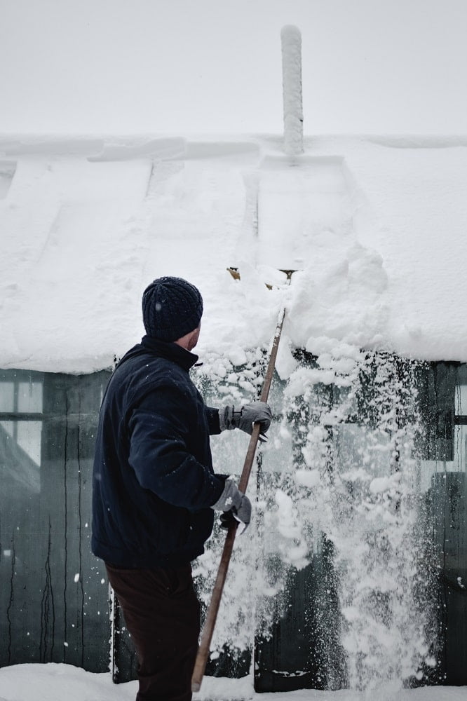 Mies kolaa lunta kasvihuoneen katolta