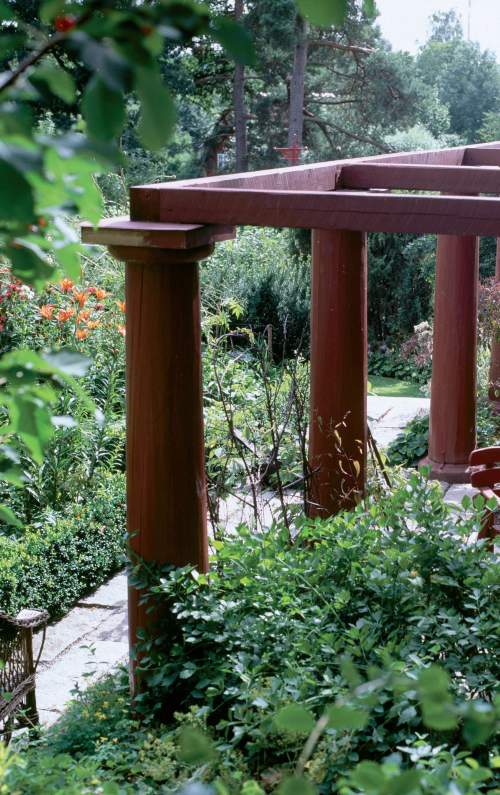 Kiinanpunaista pergolaa ympäröi rehevä puutarha. Jyhkeiden runkotolppien varaan perustettu komea rakenne ei kaipaa köynnöksiä. 