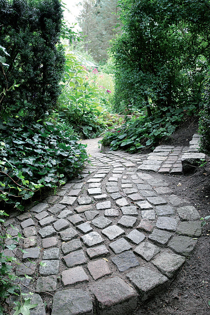 Noppakivistä ladottua käytävää reunustaa rehevä muratti (Hedera). Kiemurteleva käytävä on vastakohta puutarhan suoralinjaisille rakenteille. 